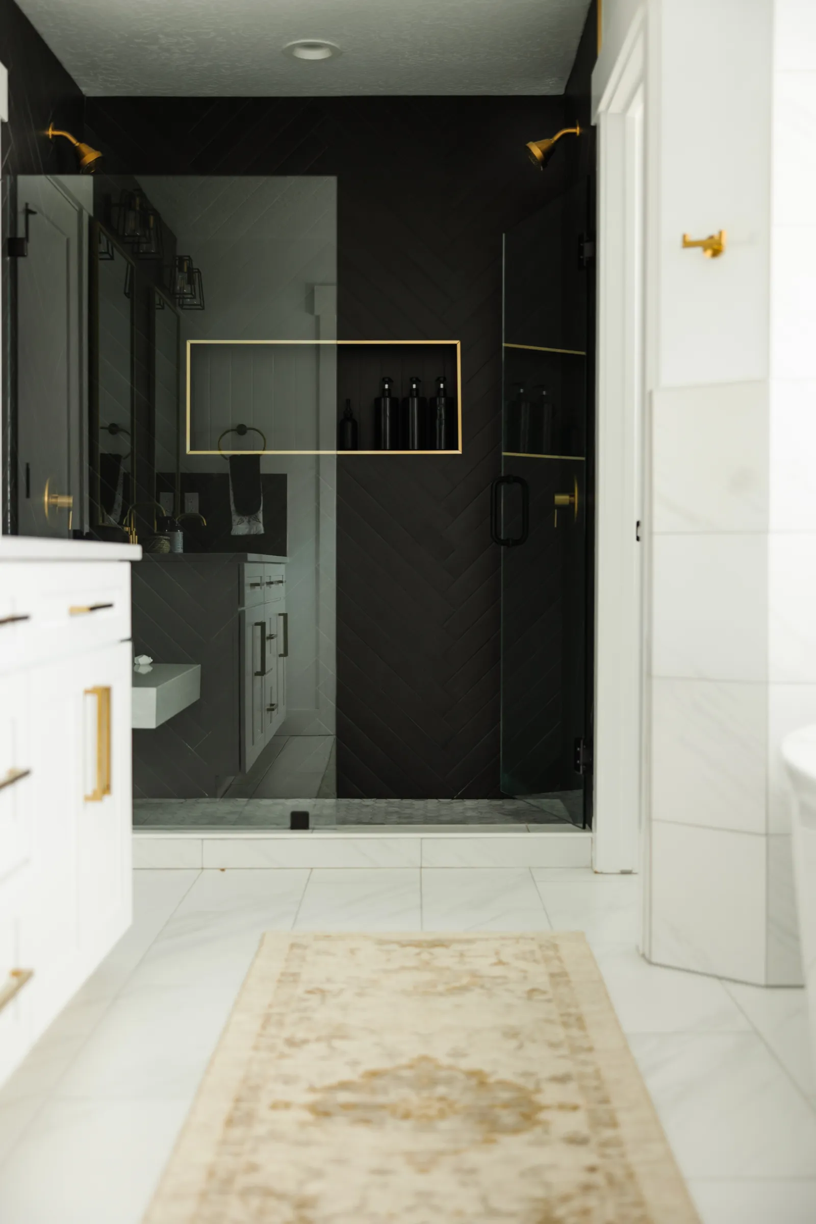 view of a marble tiled bathroom with tiled walls and glass enclosure black tiled shower, with a runner rug on the floor to prevent falling on tile floor