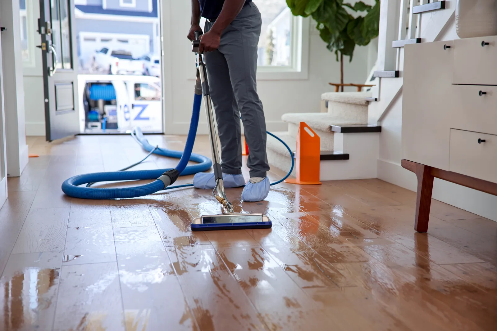 one reason why hardwood floors are slippery is because they are wet. Zerorez® technician is seen cleaning a hardwood floor in a home with the door open behind him and the Zerorez van parked outside