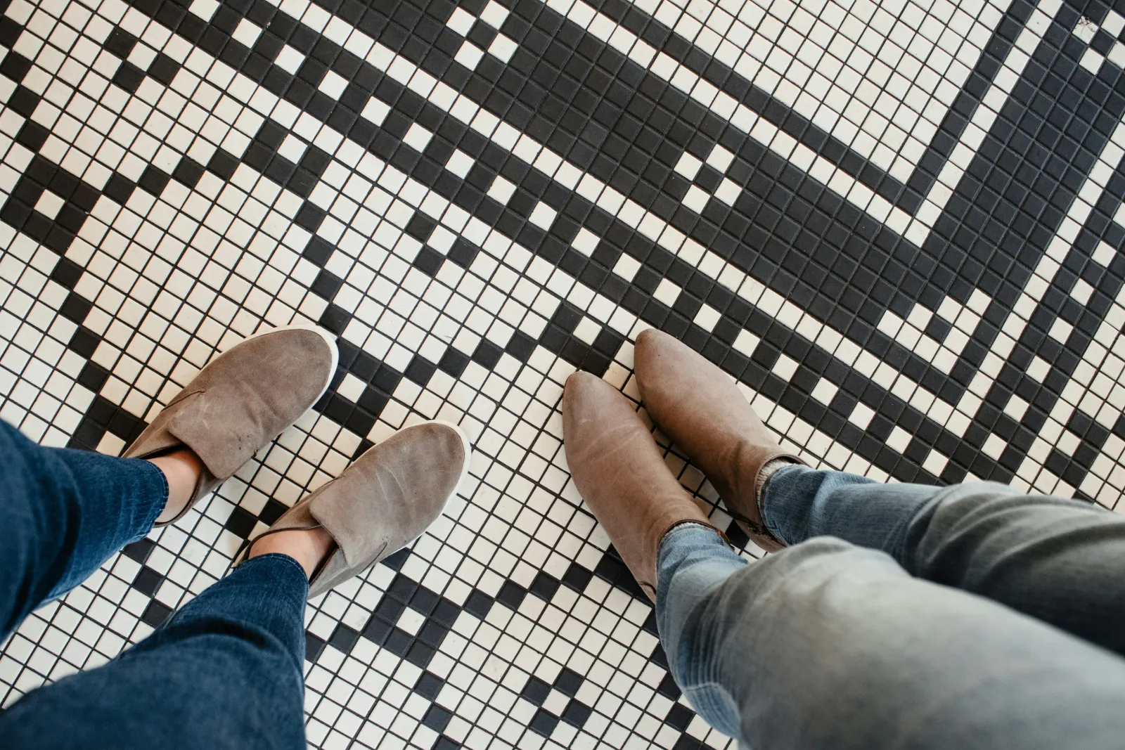 two pairs of feet and shoes standing on a black and white tile floor