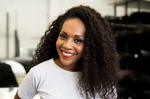 Smiling woman with curly hair wearing a white shirt standing indoors with a blurred background