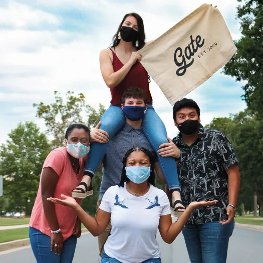 Berry students pose wearing masks holding a sign that says "GATE est. 2003"