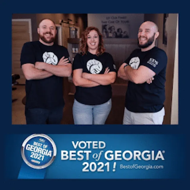 Three smiling coworkers wearing matching black t-shirts standing with arms crossed in an office setting.