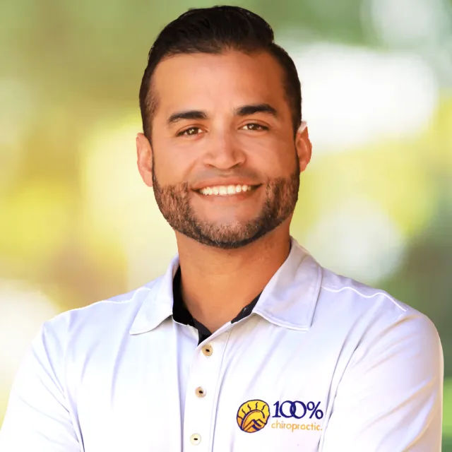 Smiling man in white 100% chiropractic polo shirt with crossed arms against blurred outdoor background
