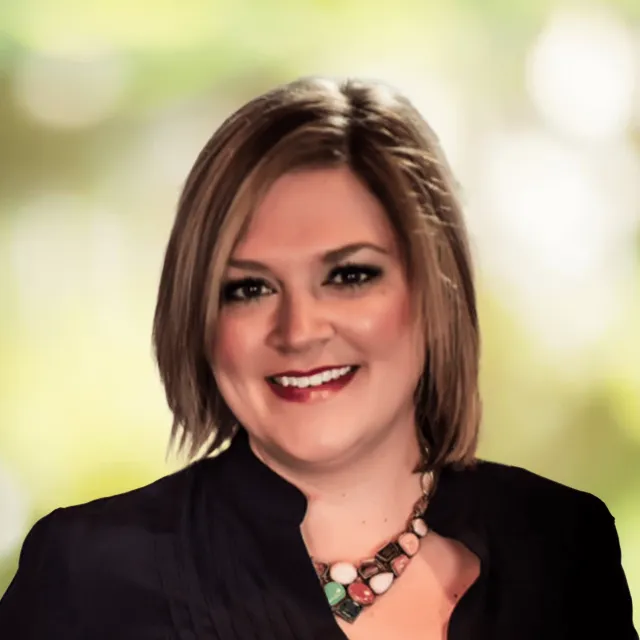 Smiling woman with short blonde hair wearing a black top and colorful chunky necklace on green blurred background