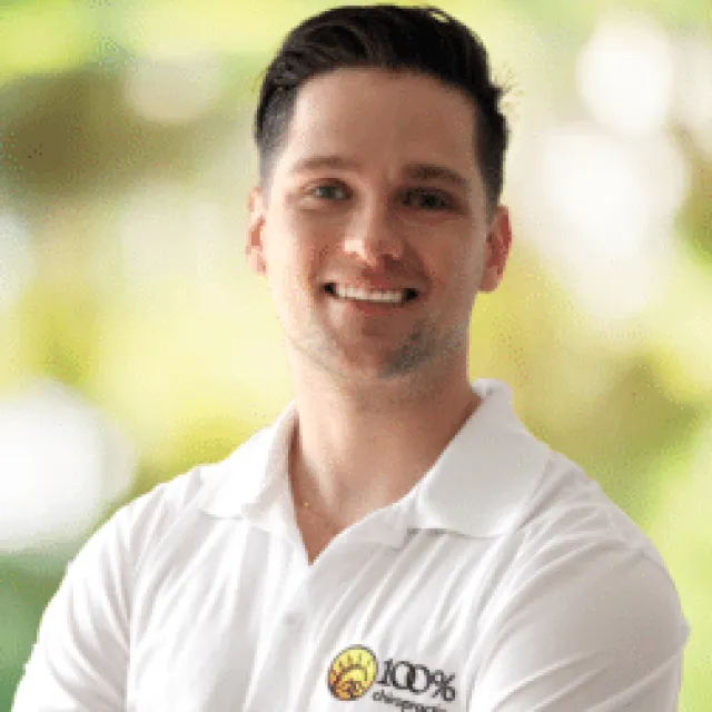 Smiling young man in white polo shirt with 100% electric logo standing outdoors with blurred green background