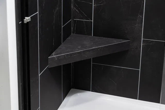Modern corner shower seat made of black marble tiles in a sleek bathroom design.