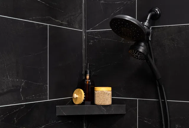 Black marble shower corner with dual showerhead and toiletries on black shelf including jar and pump bottle