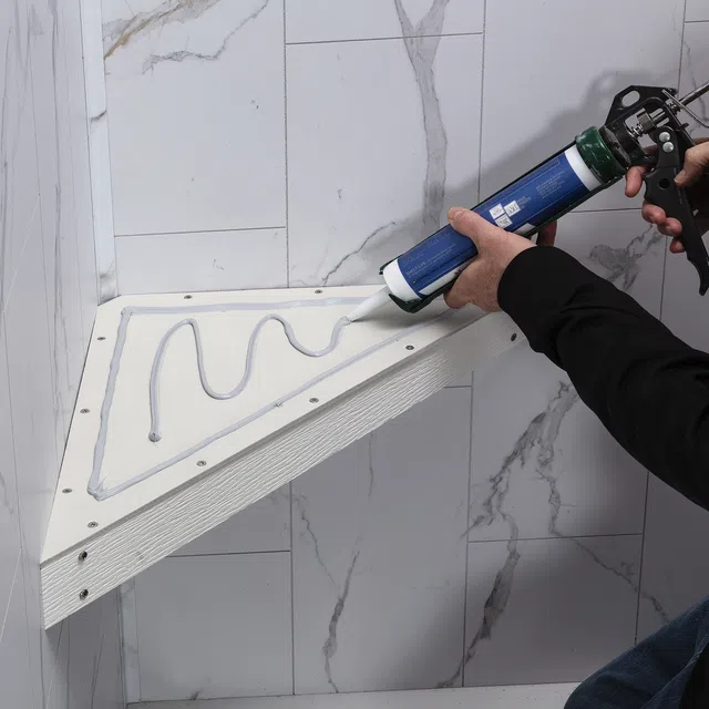 Person applying adhesive sealant to a triangular wall shelf against marble tile wall during installation.