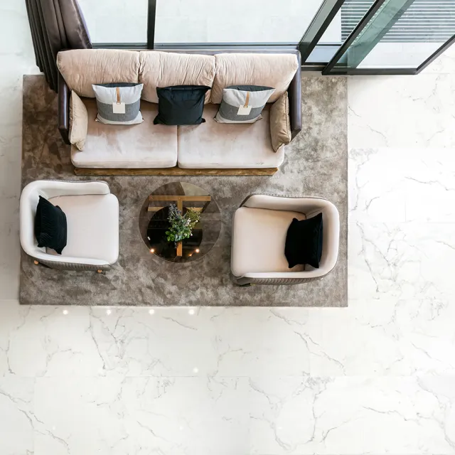 Top view of a modern living room with beige sofa, two armchairs, glass coffee table on a brown rug.