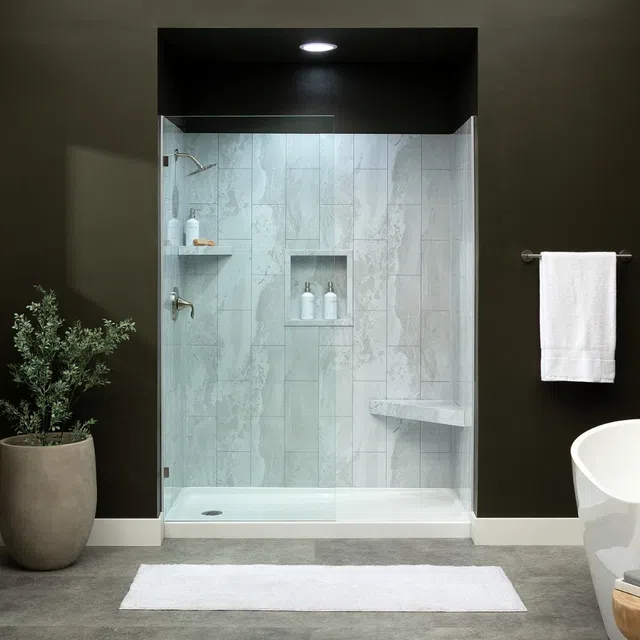 Modern walk-in shower with glass door, marble tiles, built-in shelf, bench, and dark accent walls