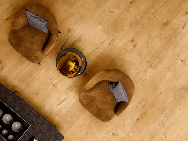 Top-down view of two brown armchairs with gray pillows and a round golden coffee table on wooden flooring.