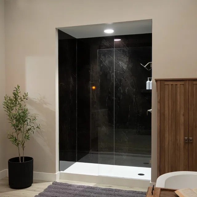 Modern bathroom with black marble shower, glass door, wood cabinet, potted plant, and gray bath rug on floor