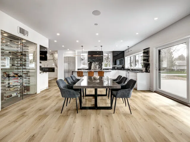 Modern open-concept kitchen and dining room with marble table, black chairs, wine rack, and large windows.