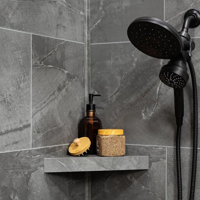 Black showerhead with hand shower and bath accessories on gray tiled wall shelf in bathroom corner