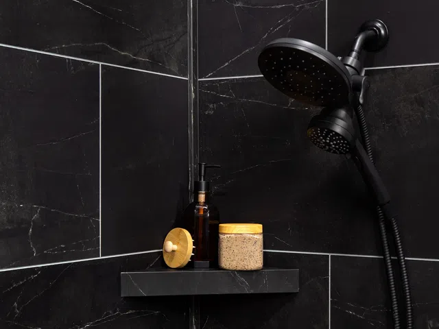 Black marble shower corner with dual showerhead and toiletries on black shelf including jar and pump bottle
