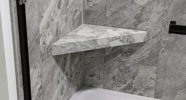 Triangular corner marble bench installed in a gray tiled bathroom shower area for storage.