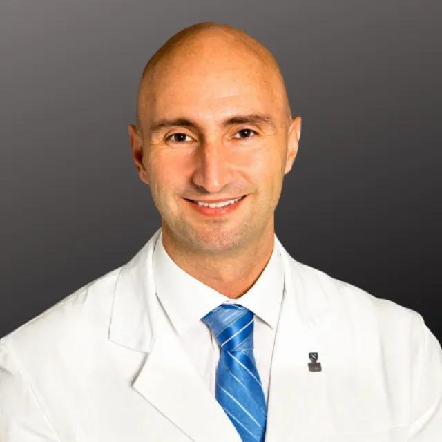 Smiling bald man in white medical coat and blue striped tie against dark gradient background