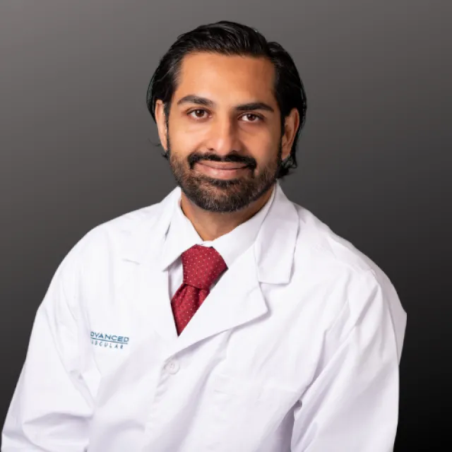 Smiling male doctor with beard wearing white coat and red tie against a dark gray background