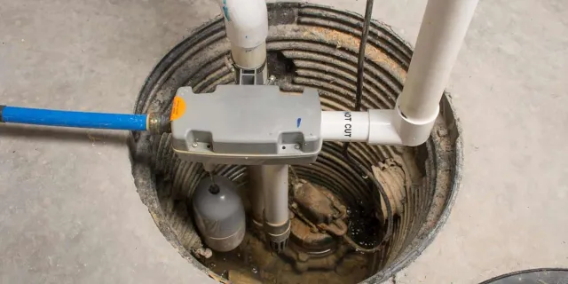 Basement sump pump system installed in a concrete pit with pipes and a float switch for water removal.