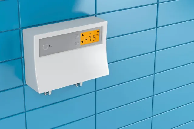 White digital thermostat mounted on blue tiled wall displaying temperature of 47.5 degrees Celsius.