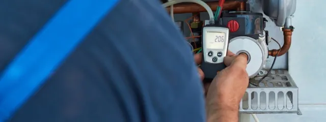 Technician using digital multimeter to test and measure electrical components on heating system equipment.