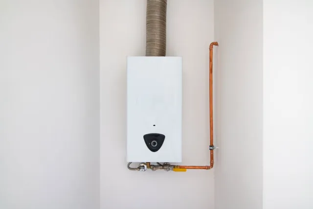 White tankless water heater mounted on wall with copper pipes and exhaust vent pipe.
