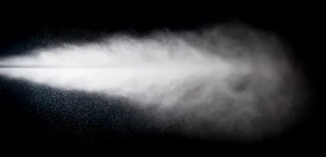 White mist or spray dispersing in the air against a black background, showing fine water droplets and vapor.