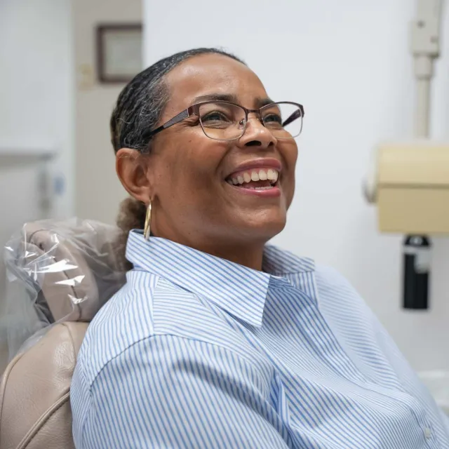 Smiling young woman with pearls and white sleeveless top in outdoor setting with blurred green background