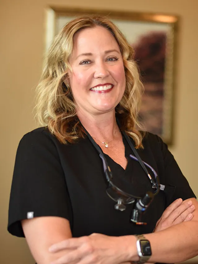 Smiling female dentist in a black uniform with dental tools, showcasing confidence and professionalism.