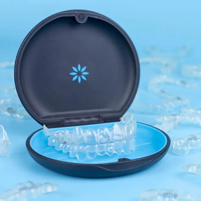 Transparent dental aligners in an open black and blue case on a blue background with scattered aligners.