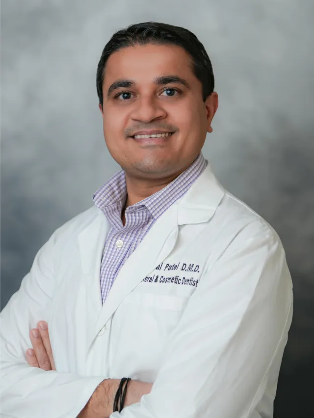 Smiling dentist in a white coat, looking confident against a soft gray background.