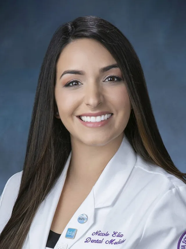 Smiling female dental medic in a white coat with name badge and dental association pins on a blue background