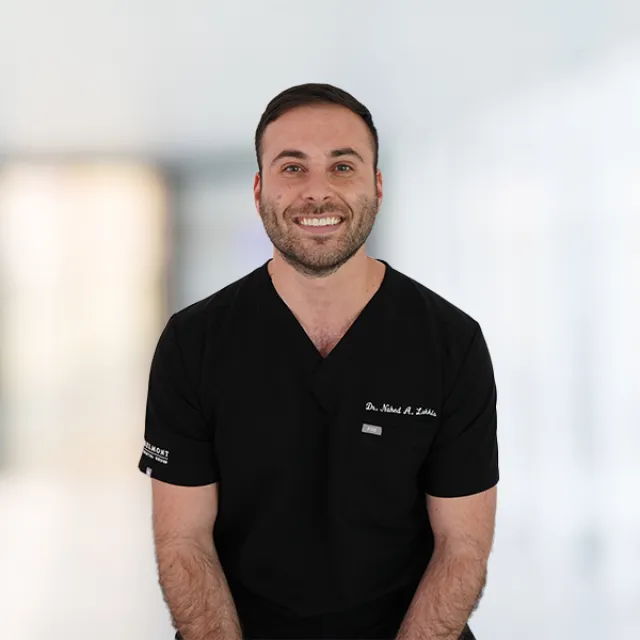Smiling male healthcare professional in black scrubs standing in a bright blurred medical office background