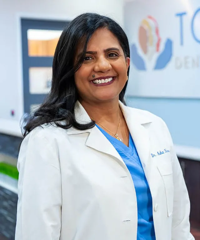 Smiling female dentist in white coat and blue scrubs standing inside dental clinic.