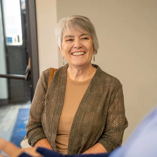 Smiling elderly woman with gray hair chatting warmly with a person in a blue shirt indoors