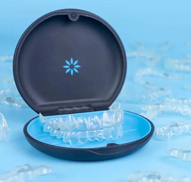 Transparent dental aligners in an open black and blue case on a blue background with scattered aligners.