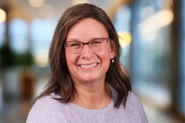 Smiling woman wearing blue glasses and a light gray fleece jacket with a Rip Curl logo on black background