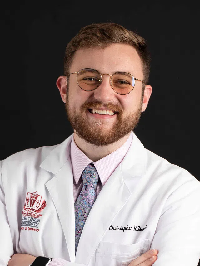 Smiling male dentist wearing glasses and a white lab coat with Loma Linda University School of Dentistry logo