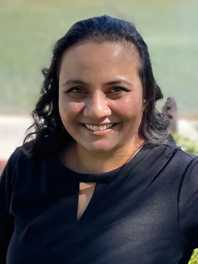 Smiling woman with wavy dark hair wearing a black top outdoors in bright sunlight