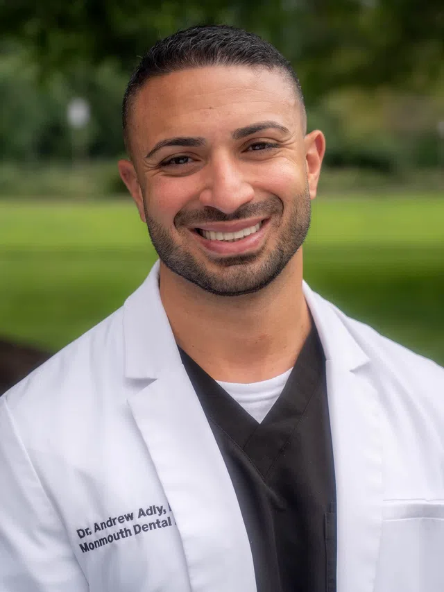 Smiling male healthcare professional wearing a white coat and black scrubs in an office setting