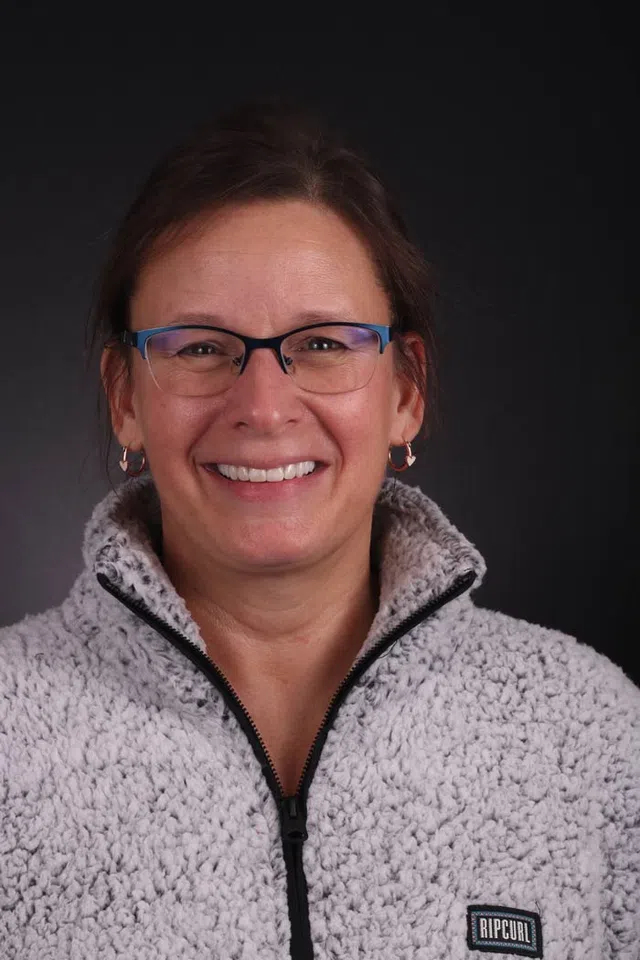 Smiling woman wearing blue glasses and a light gray fleece jacket with a Rip Curl logo on black background