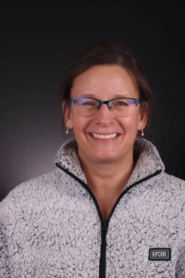 Smiling woman wearing glasses and a gray Ripcurl fleece jacket against a dark background