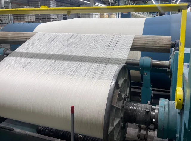 Large industrial textile machine tightly winding white thread onto a spool in a factory setting.