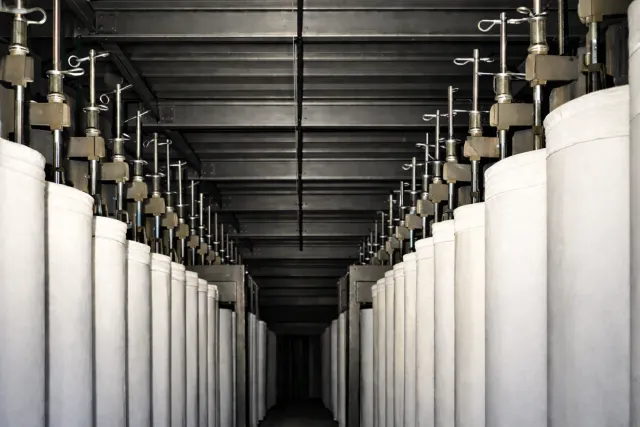 Rows of industrial fabric filter bags hanging in a factory setting with metal supports and ceiling structure.