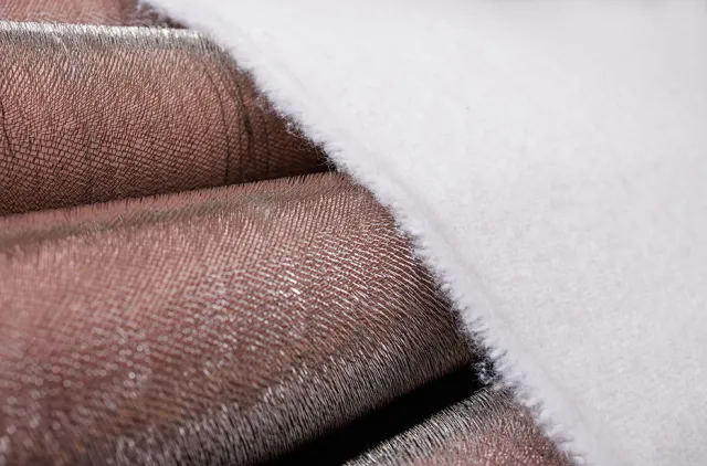 Close-up of soft, textured fabric with a shiny metallic brown surface partially covered by white fuzzy material.