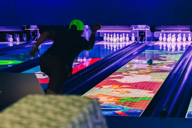 Person wearing a neon green cap bowling in a lane with colorful projections under blacklight