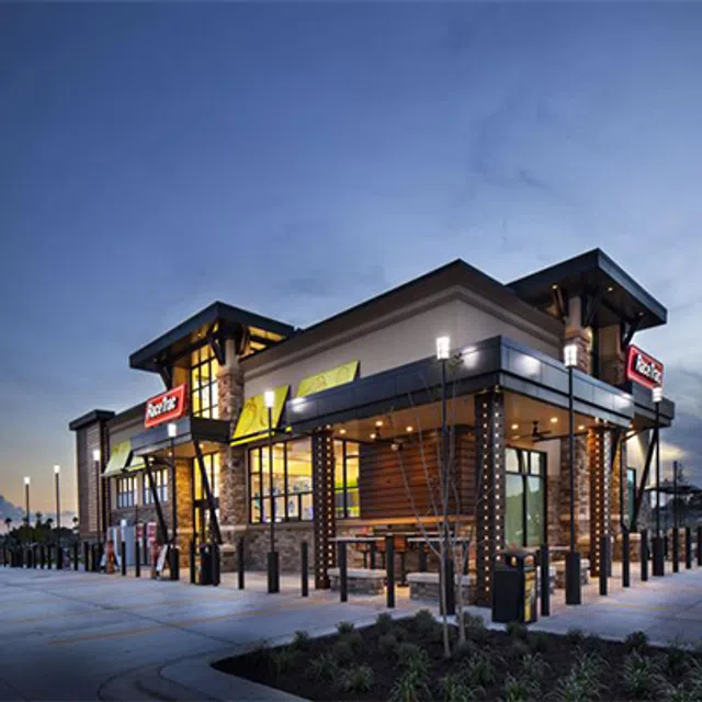Modern fast-food restaurant building with outdoor seating and illuminated signage at dusk under a clear sky