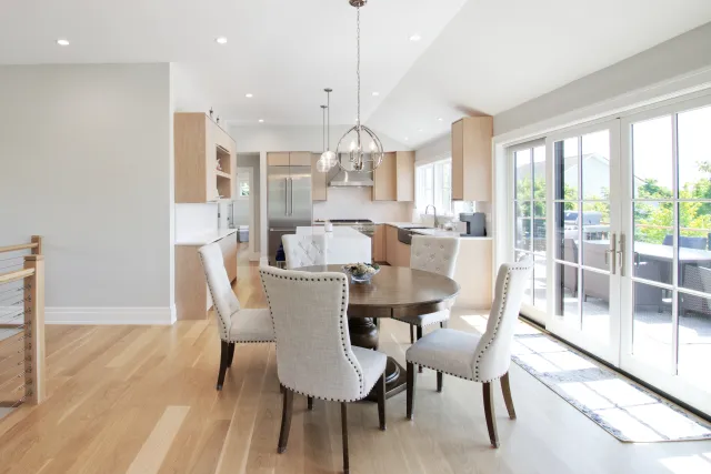 Bright modern dining area with round wooden table, four upholstered chairs, and sliding glass doors to patio
