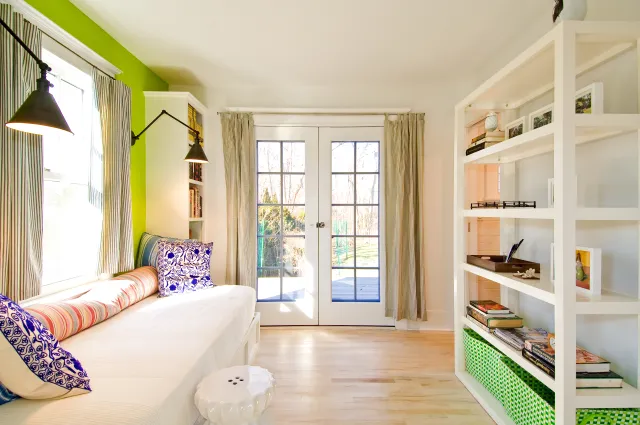 Bright room with white built-in sofa, colorful pillows, green accent wall, and French doors leading outdoors