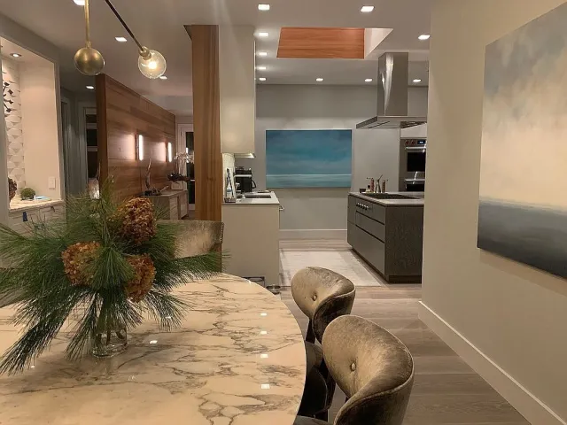 Modern dining area with marble table, velvet chairs, pine centerpiece, and view into sleek kitchen and abstract art.